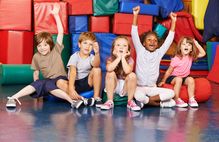 Bild zeigt Kinder, die in der Sporthalle sitzen; Schaltfläche zum Themenfeld Schule und Verein