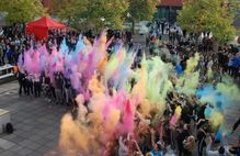 Bild zeigt Kindermenge, die Farben in die Luft werfen; Schaltfläche zum Sportjugendangebot Step it up Festival